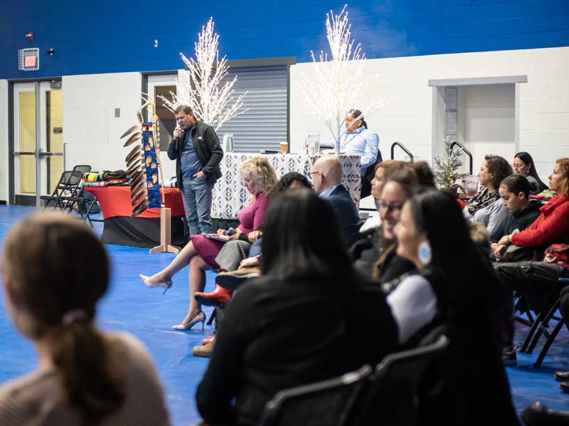 Harvey Dreaver stands at the front of the room in front of the audience while speaking into a microphone.